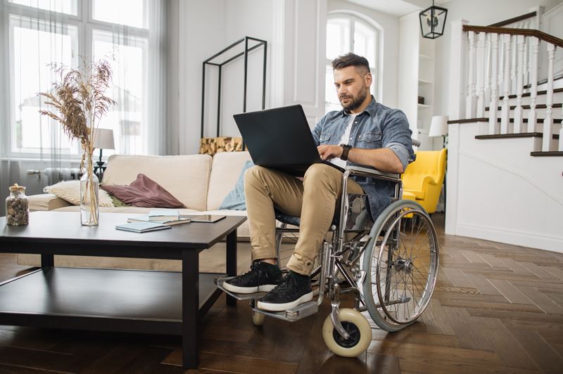 Young,Male,Wheelchair,User,In,Casual,Clothes,Looking,At,Laptop