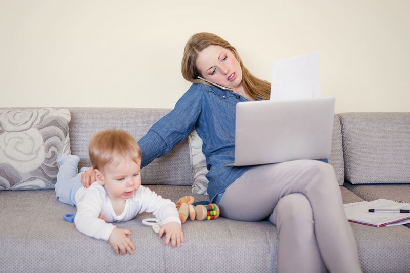 Working,Mom,With,Baby,On,The,Couch,,Working,On,Laptop