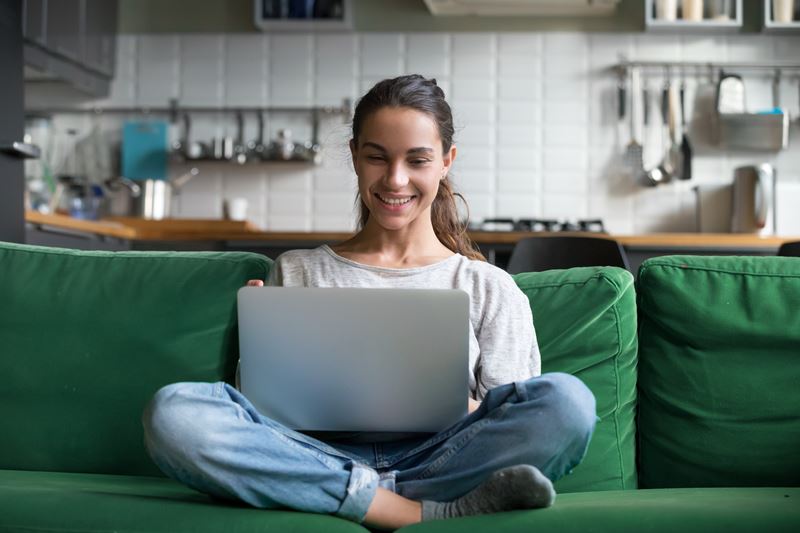 Happy smiling woman sitting on sofa and using laptop